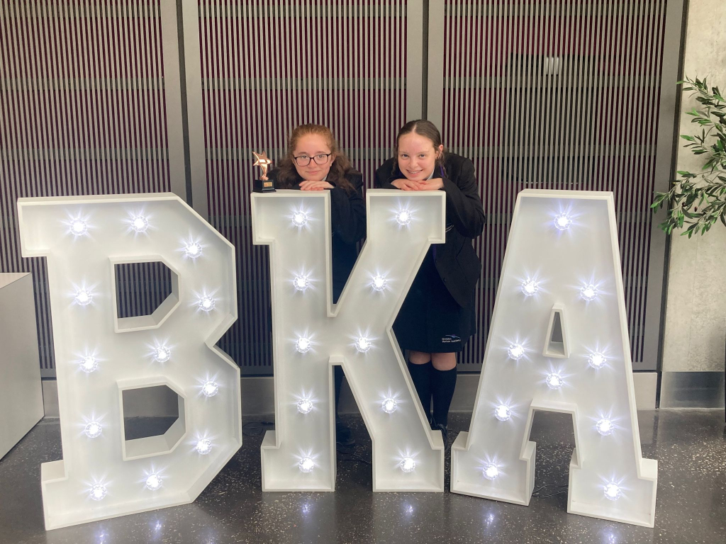 students at awards behind be kind logo